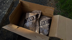 Open cardboard box with bags of肥料 on a grassy path